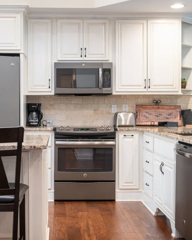Modern kitchen with white cabinetry, stainless steel appliances, granite countertops, tile backsplash, and hardwood flooring.
