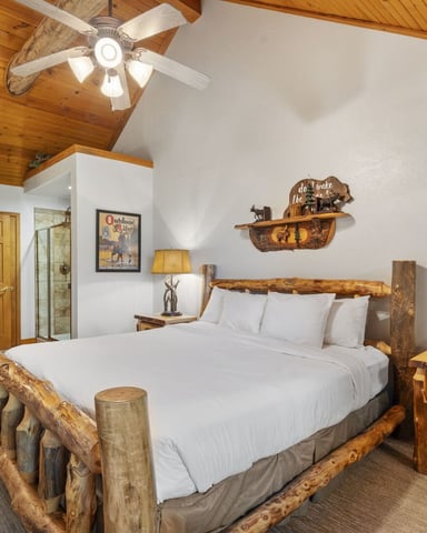 Rustic bedroom with log bed frame, white bedding, wooden ceiling, ceiling fan, and outdoor-themed wall decor