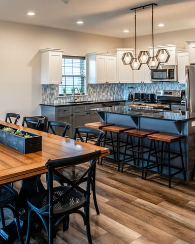 Open-plan kitchen and dining area with wood table, blue chairs, white cabinetry, blue tile backsplash, and stainless steel appliances.