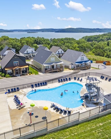 Residential community with swimming pool, playground, and tennis court overlooking a large lake and forested shoreline