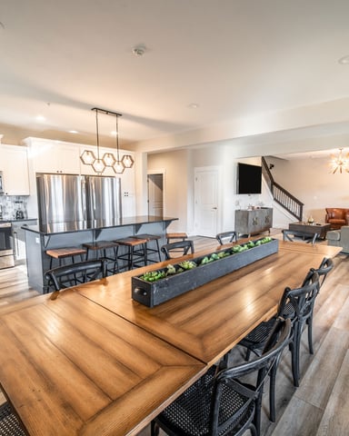 Open-plan kitchen and living area with wood dining table, white cabinetry, stainless steel appliances, and stairs to upper level