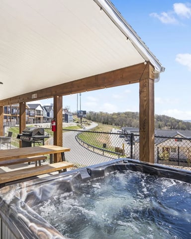 Covered patio with hot tub, picnic table, and expansive view of lake and residential neighborhood below