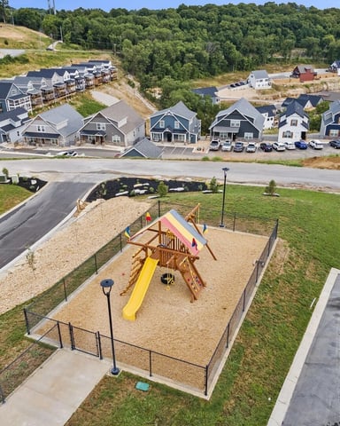 Aerial view of residential development with playground, houses, and forested hillside in background
