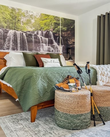 Bedroom with wooden bed, green quilted bedding, woven storage ottomans, and large waterfall mural headboard with forest view.