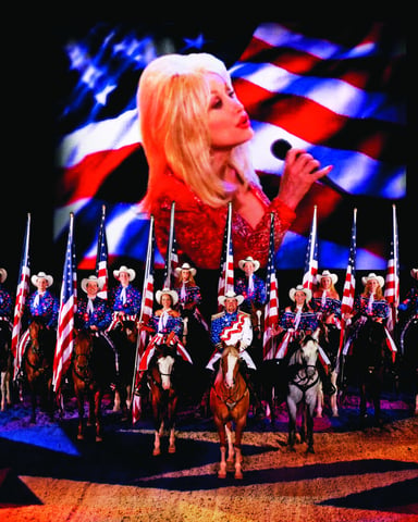 Performers on horseback holding American flags with a singer projected on screen behind them during a patriotic stage show
