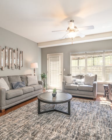 Bright living room with gray upholstered sofas, round coffee table, hardwood floors, and glass doors opening to patio