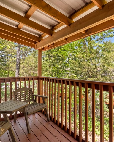 Covered wooden deck with metal chairs overlooking dense forest canopy and trees