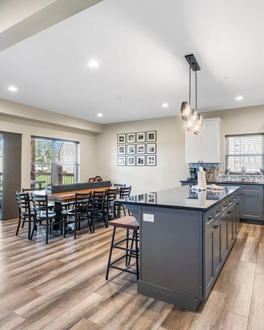 Open-plan kitchen and dining area with dark island, stainless steel appliances, and glass doors opening to deck