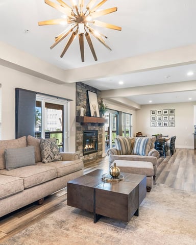 Open-plan living room with beige sofa, fireplace, and kitchen visible in background, modern starburst ceiling light fixture overhead