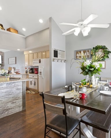 Open-plan kitchen and dining area with island, dining table, white ceiling fan, and fresh flower arrangement
