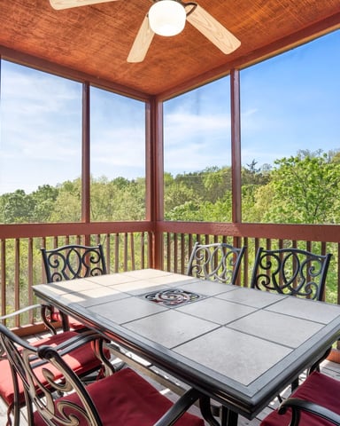 Screened porch with wood ceiling, dining table, ornate chairs, and expansive forest views