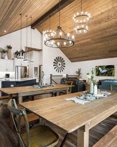 Open-plan kitchen, dining, and living area with wood ceiling, white cabinetry, wooden tables, and blue seating