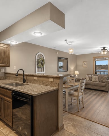 Open-plan kitchen and living room with granite countertops, wood cabinetry, and lake view through glass doors
