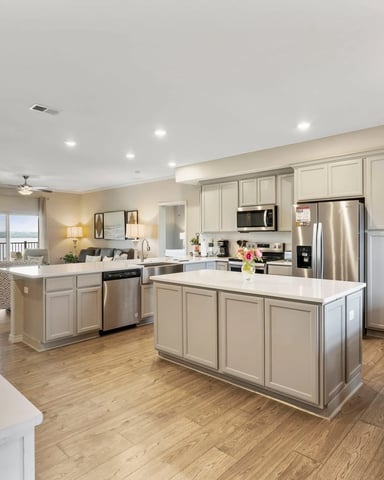 Open-plan kitchen and living area with cream cabinetry, stainless steel appliances, two islands, and water view through sliding glass doors.