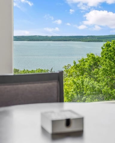 Dining table with lake view through large windows, green hillside and blue water visible beyond