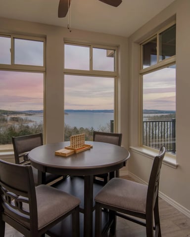 Dining room with round table, four chairs, and expansive windows overlooking a lake at sunset