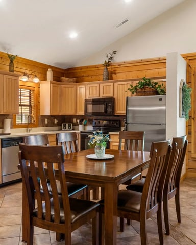 Open-plan kitchen and dining area with wood cabinetry, stainless steel appliances, dining table with four chairs, and glass doors to outdoor patio.
