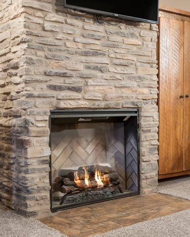 Stone fireplace with gas fire insert and TV mounted above, wooden furniture and cabinetry flanking sides