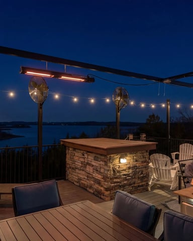 Illuminated rooftop deck at dusk with stone bar, grill, seating, and lake view beyond railing
