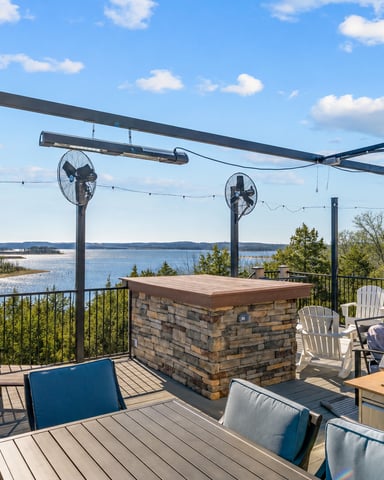 Elevated deck with lake view, stone bar, grill, Adirondack chairs, and overhead fans under pergola
