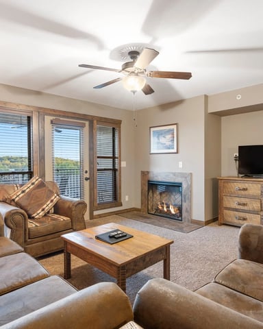 Spacious master bedroom with sitting area, fireplace, large windows overlooking landscape, and ceiling fan