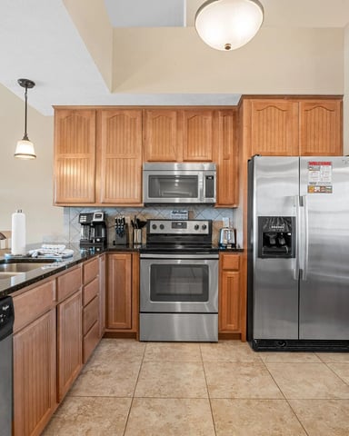 Kitchen with wood cabinetry, stainless steel appliances, black granite countertops, and tile flooring