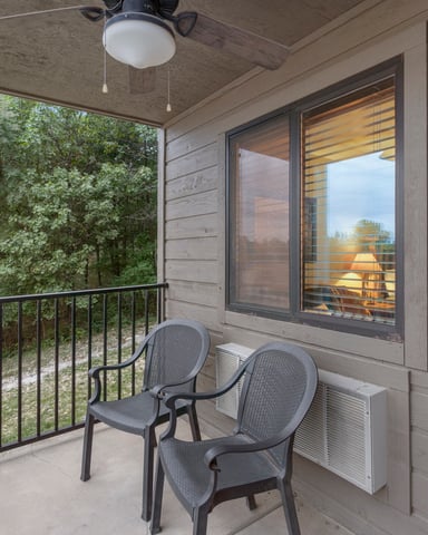 Covered porch with two dark chairs, metal railing, and forest view through open side