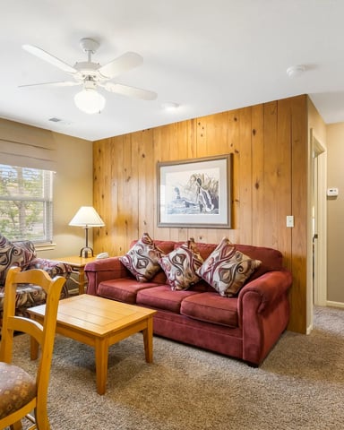 Living room with red sofa, patterned armchair, wood paneling, ceiling fan, and framed artwork on walls