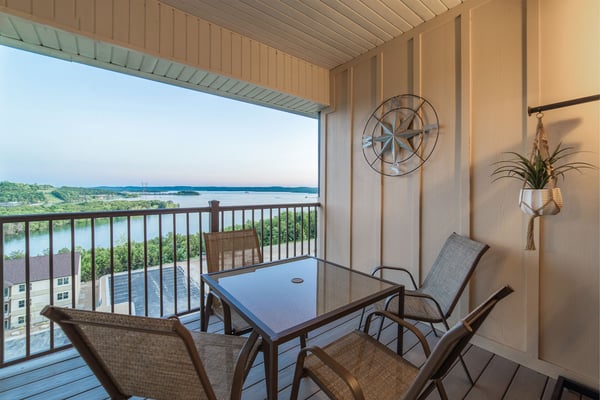 Covered balcony with dining table, chairs, and lake view through railing, metal fan and hanging plant on wall